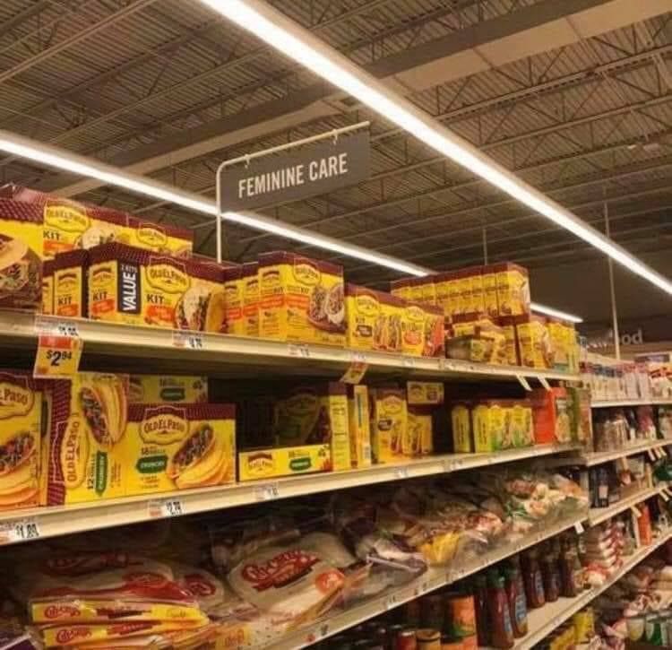 A grocery store shelf labelled "feminine care" and stocked with taco kits