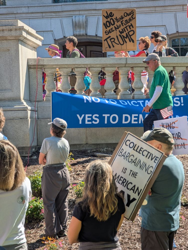 Protesters in front of the Wisconsin State Capitol building, including a cardboard sign with the words painted on it, 