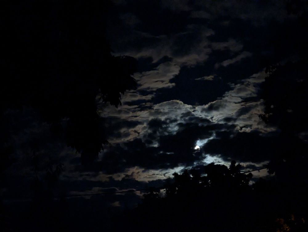 The full moon peeking through mostly cloudy skies