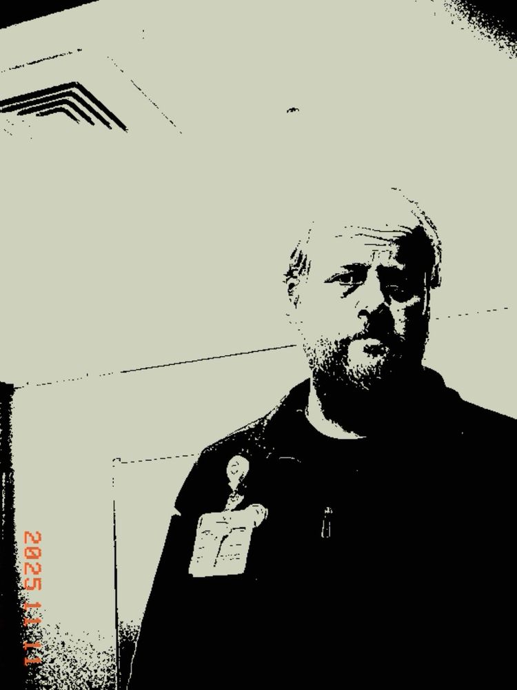 Kodak Charmera monochrome image - a mirror selfie of a bearded white guy dressed in black, a wary expression on the face