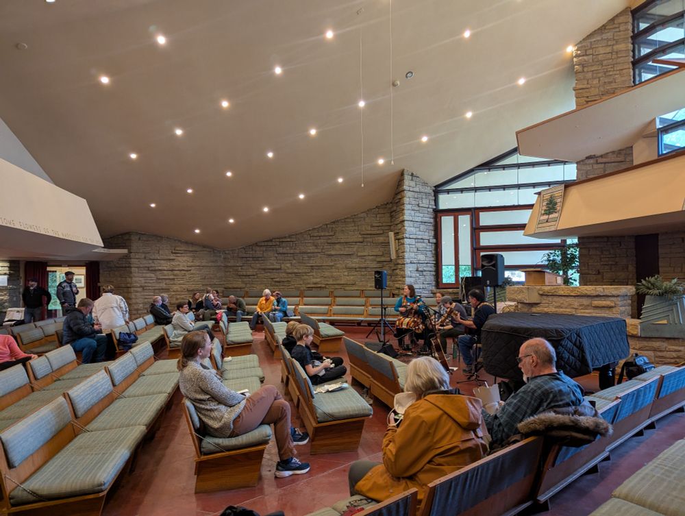 Interior of the society sanctuary, people are sitting on pews eating lunch and listening to Irish folk music