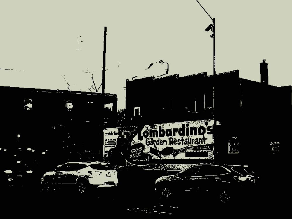A Kodak Charmera monochrome image of a building with a mural on the side advertising "Lombardino's Garden Restaurant", with cars on the street in the foreground