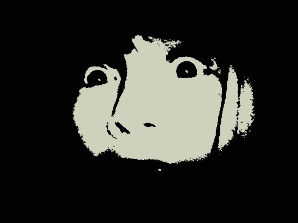 A Kodak Charmera monochrome image of a child's wide eyes and an oval of light on the middle of their face, with all else black