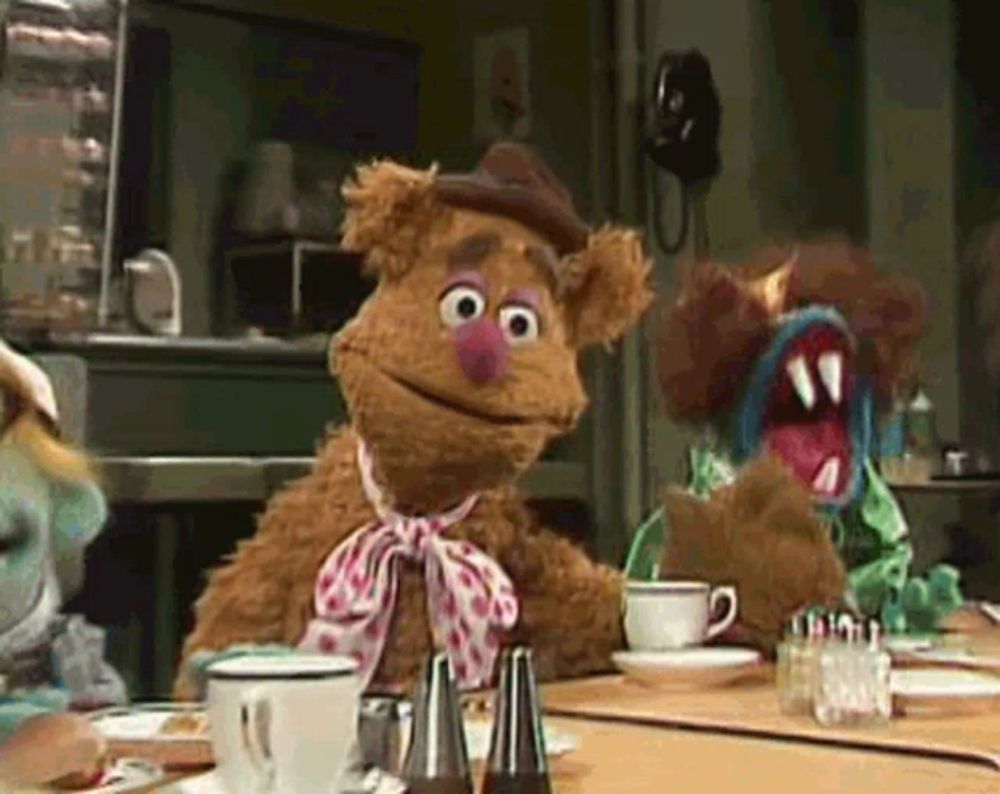 fozzie bear is sitting at a table with a cup of coffee