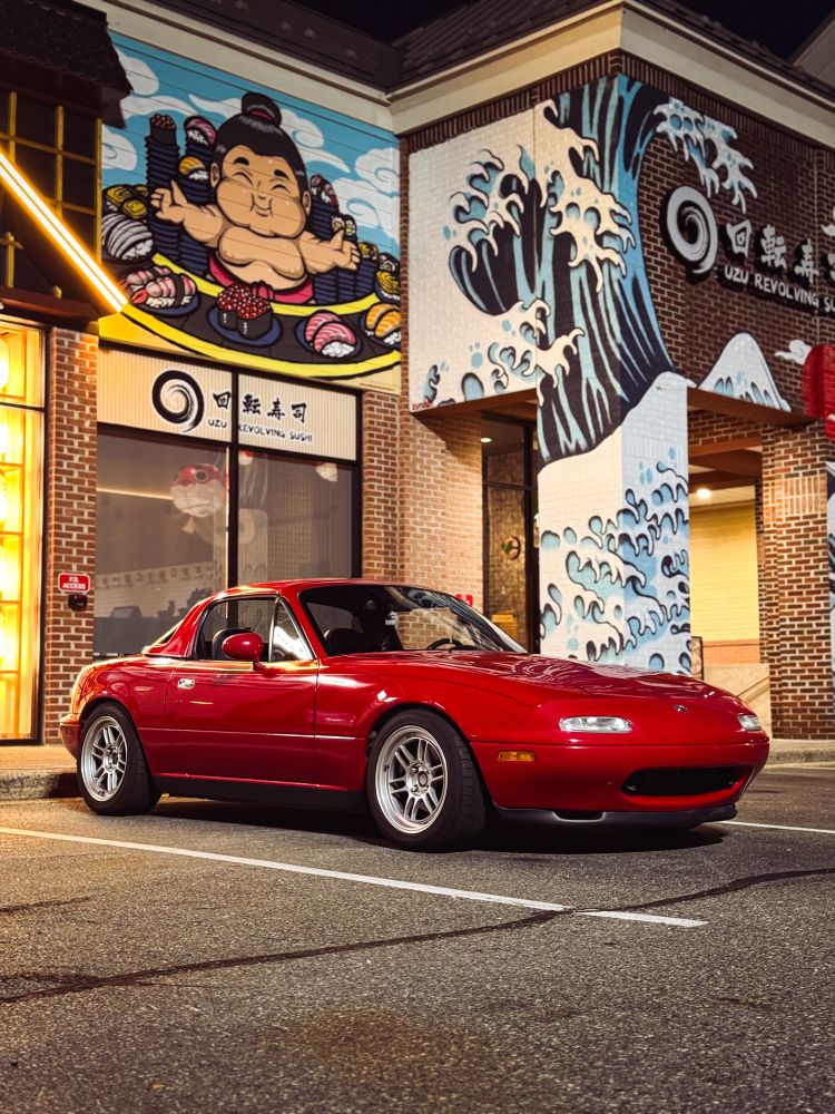 Red NA MX5 Miata with a hardtop and Enkei wheels in front of a Japanese themed mural 
