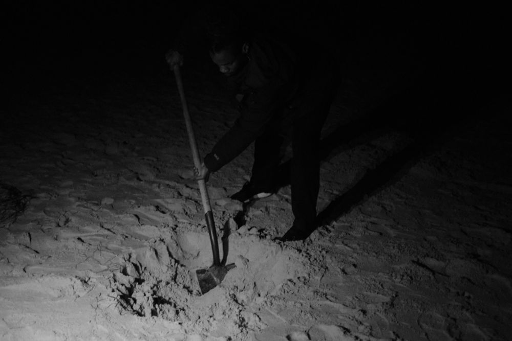 A photo of Blue from Pigeonwing dance company digging a hole on a beach