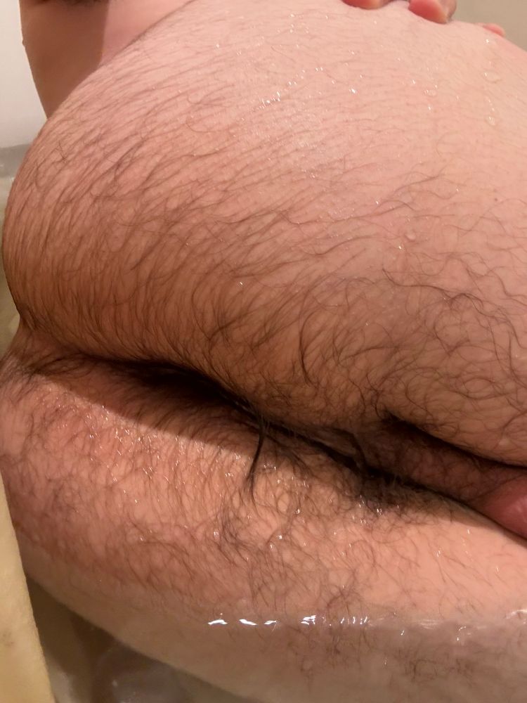 Picture of a naked person in a bath, showing off his hairy hole, legs closed. 