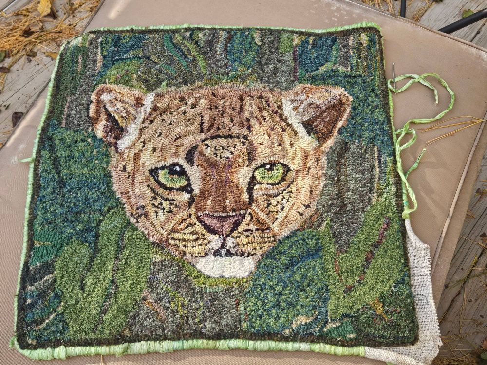 Rug hooked imaged of a leopard with bright green eyes emerging from leaves