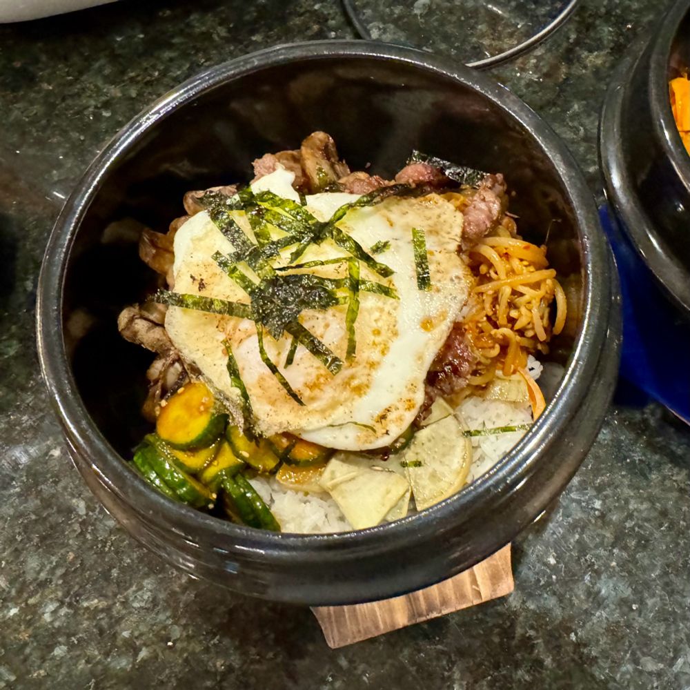 Stone Pot Bibimbap with various vegetables, marinated beef, and a fried egg on top.