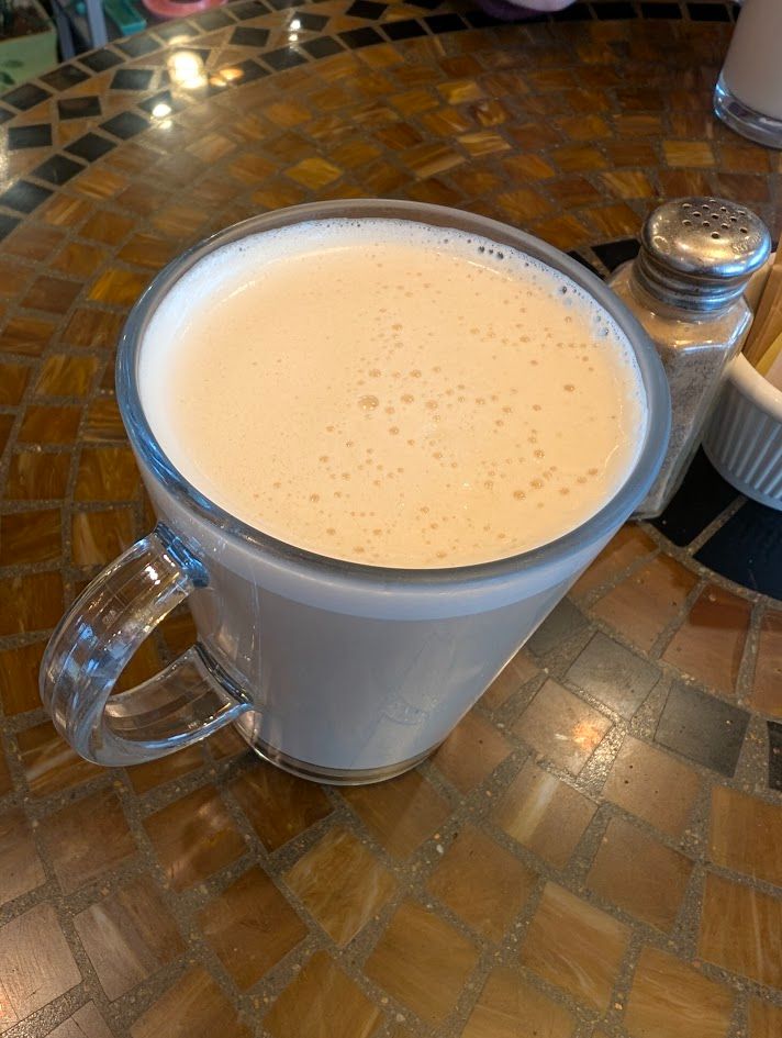 A chai latte on a brown, square tiled table