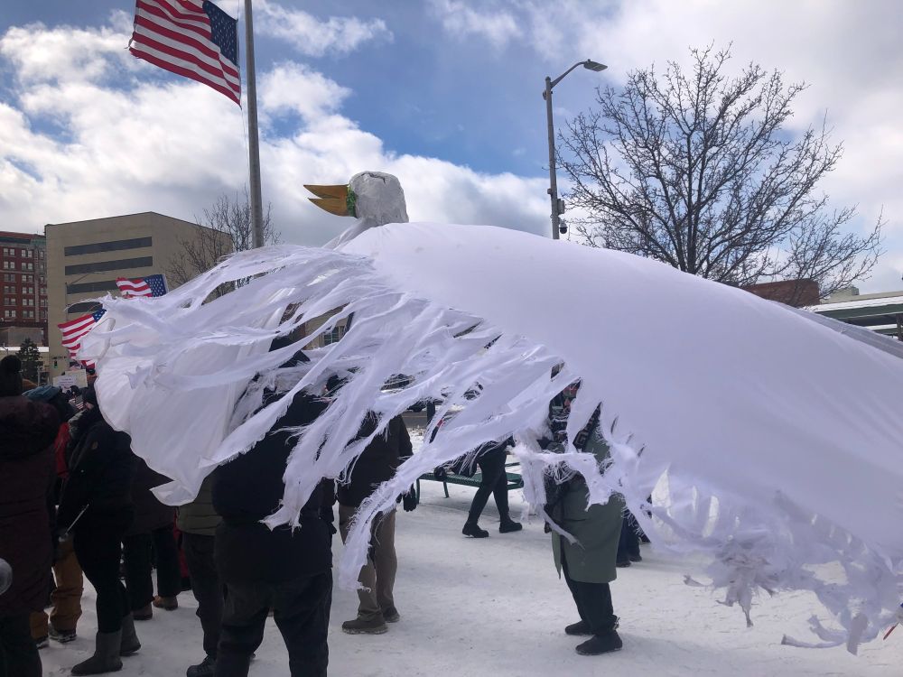 A peace-dove puppet made from papier-mache and a sheet blows in the wind over some protesters. 