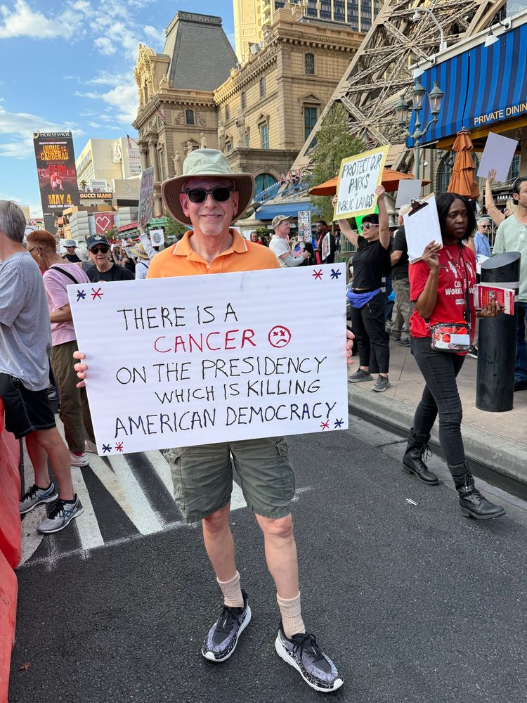 Man holding sign “There is a cancer on the presidency which is killing democracy,” at the Las Vegas Protest on May 1, 2025. 