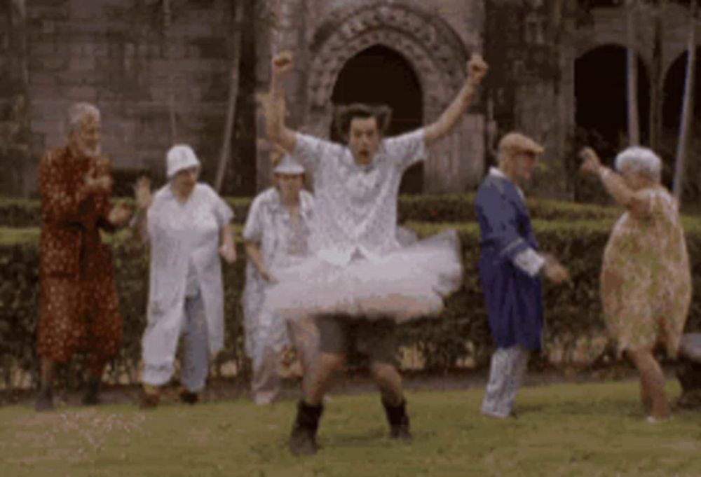 a group of elderly people are dancing in a park with a man in a tutu