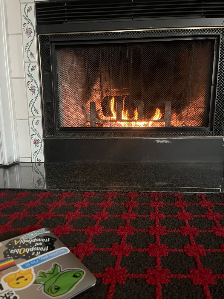 A corner of a MacBook shown on the floor on a black and red checked rug in front of a fireplace.