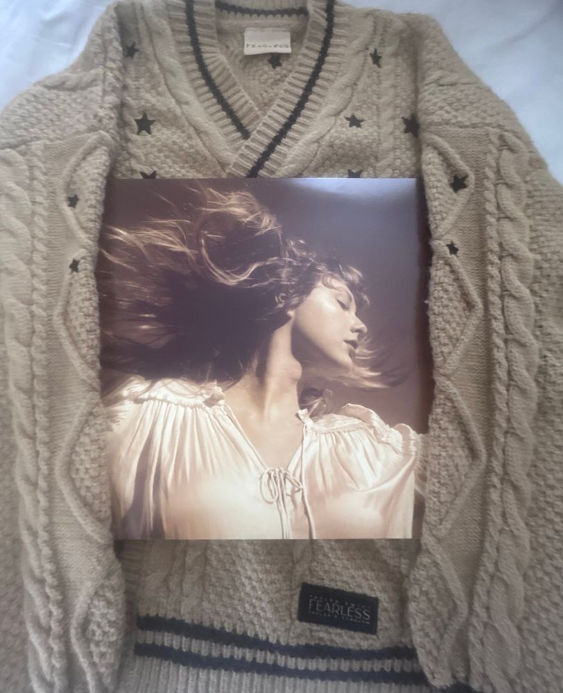 a photo of a tan cardigan with black stars with a Fearless Taylor’s Version vinyl album cover in the middle. 