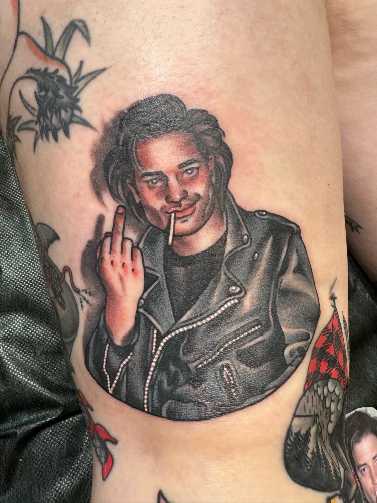 A tattoo portrait of a paparazzi picture of Brendan Fraser, drunk in a leather jacket while smirking and holding up his middle finger.
