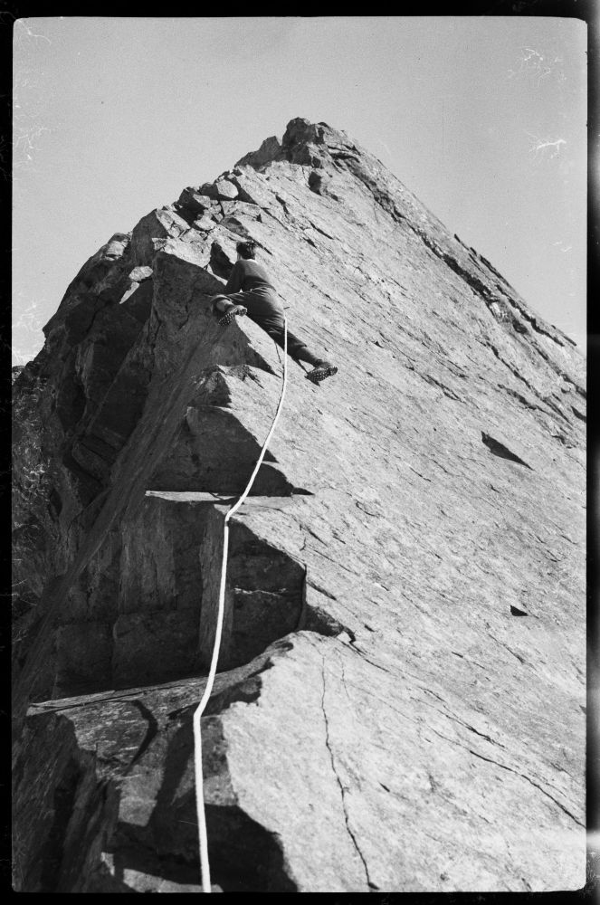 A climber on a narrow rockface photographed from below