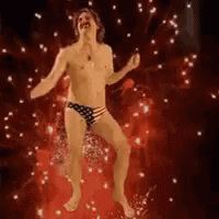 A still from the gif of a man in an American flag speedo dancing with fireworks in the background. 