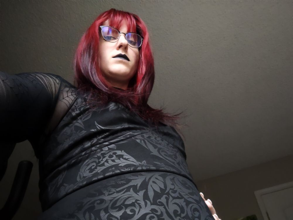 Robin looking down at the camera with a disappointed look. Wearing a floral patterned black dress with mesh spiderweb top