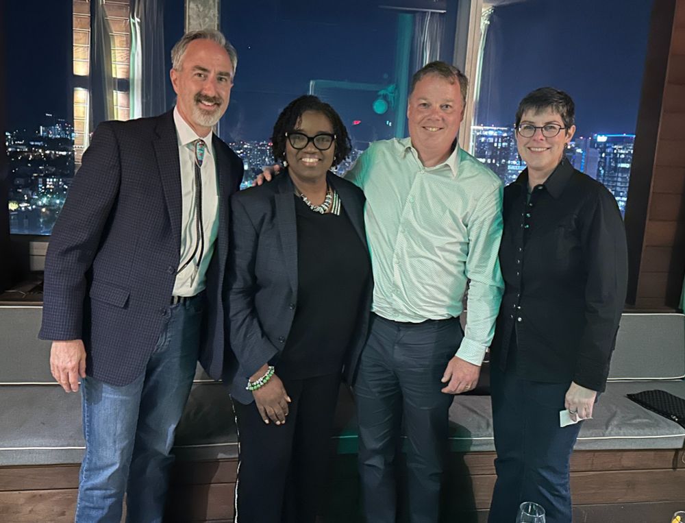 Photo of a group of four people, two men and two women, in front of a window in a skyrise, with the city behind them. The photo features (left to right) Commissioner Ben Boggs of MO Dept. of Higher Education and Workforce Development; President Avis Proctor of Harper College; NCHEMS President Brian Prescott; and President Tracy Hartzler of Central New Mexico Community College. 