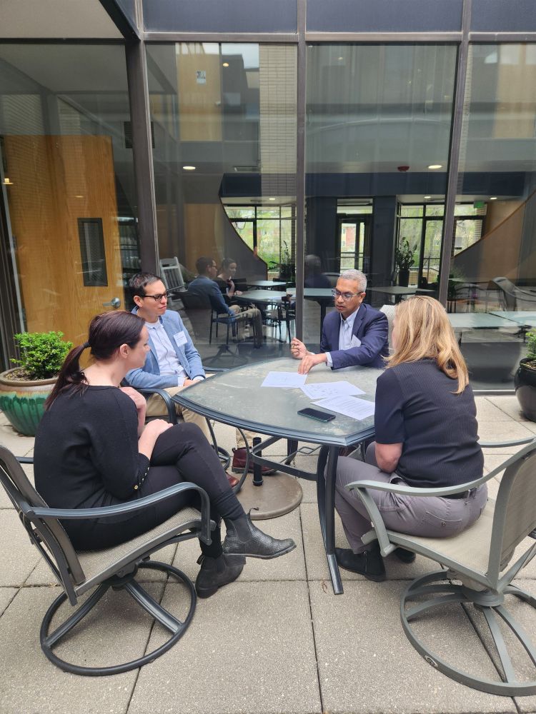 Photo of a group of four people working outside at a table in discussion. 