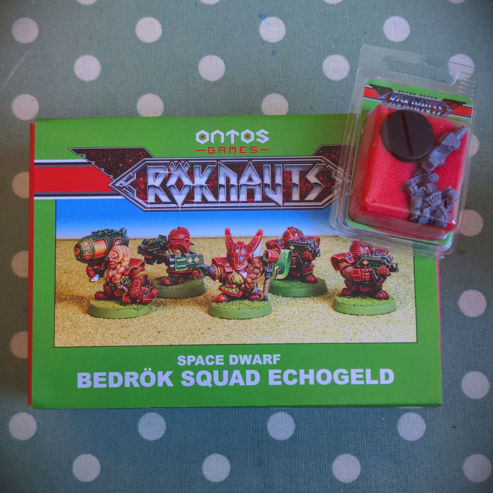 A brightly coloured box in red and green with a picture of some miniature space dwarfs on it and a small blister pack in the corner.
