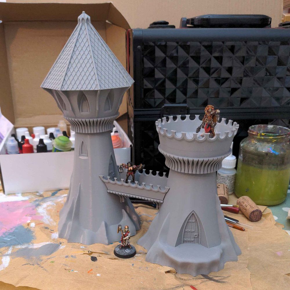 An unpainted grey 3D printed model of an elven watchtower with a some miniatures on it.. sitting on a messy desk.