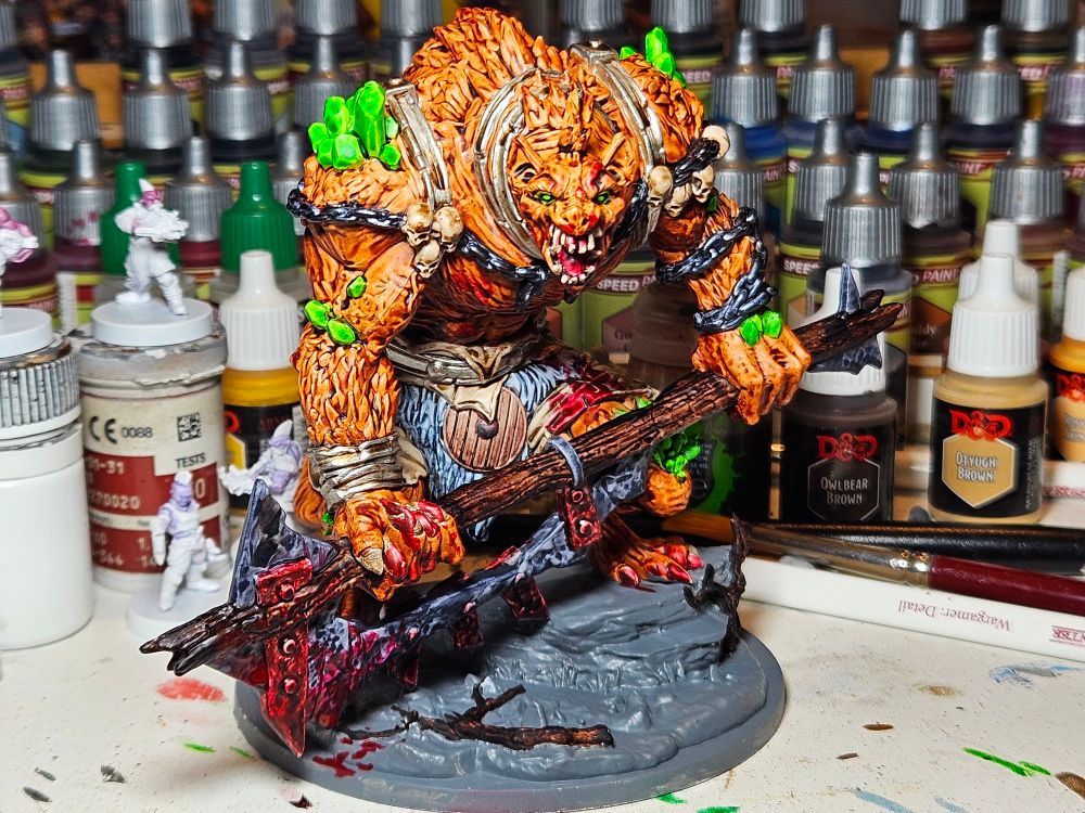 Dnd miniature depicting a giant hyena-man holding a huge scrap metal axe. The gnoll has green crystals growing out of its bloody fur and glowing green eyes. 