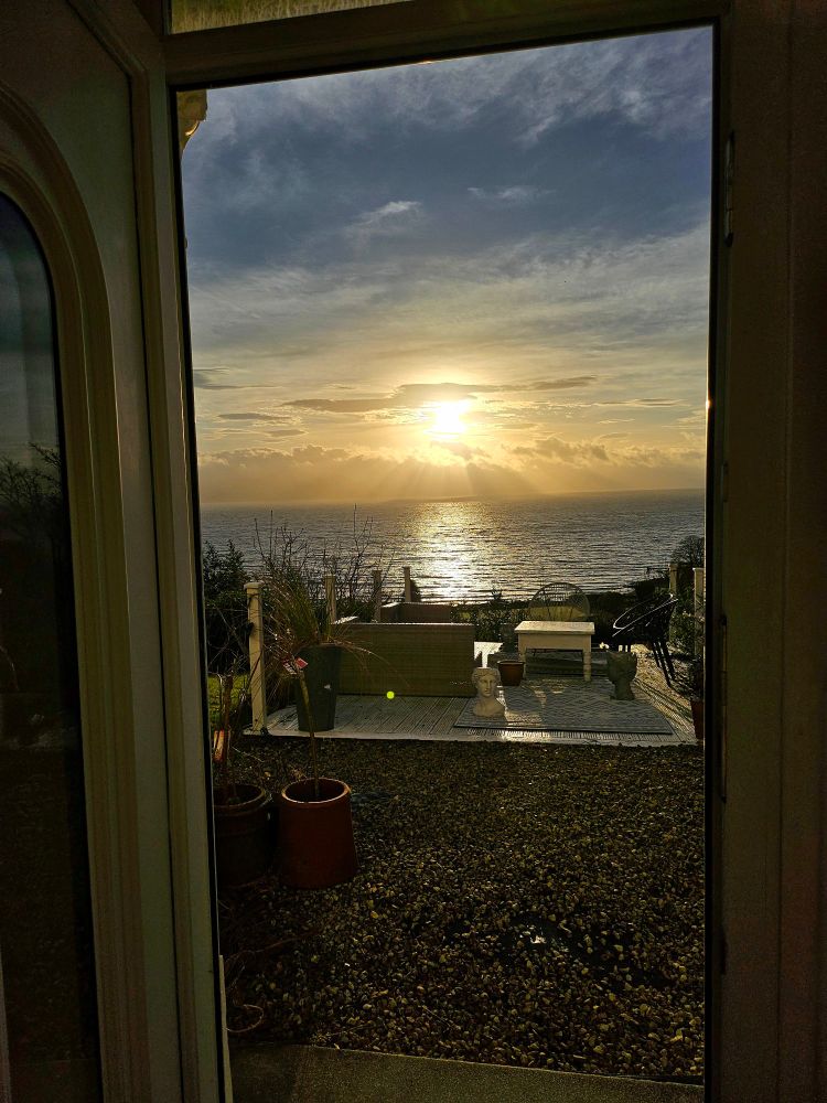 A view from my doorstep over the Firth of Clyde two hours later. The bright sun is central, with blue sky above and a yellow glow beneath.