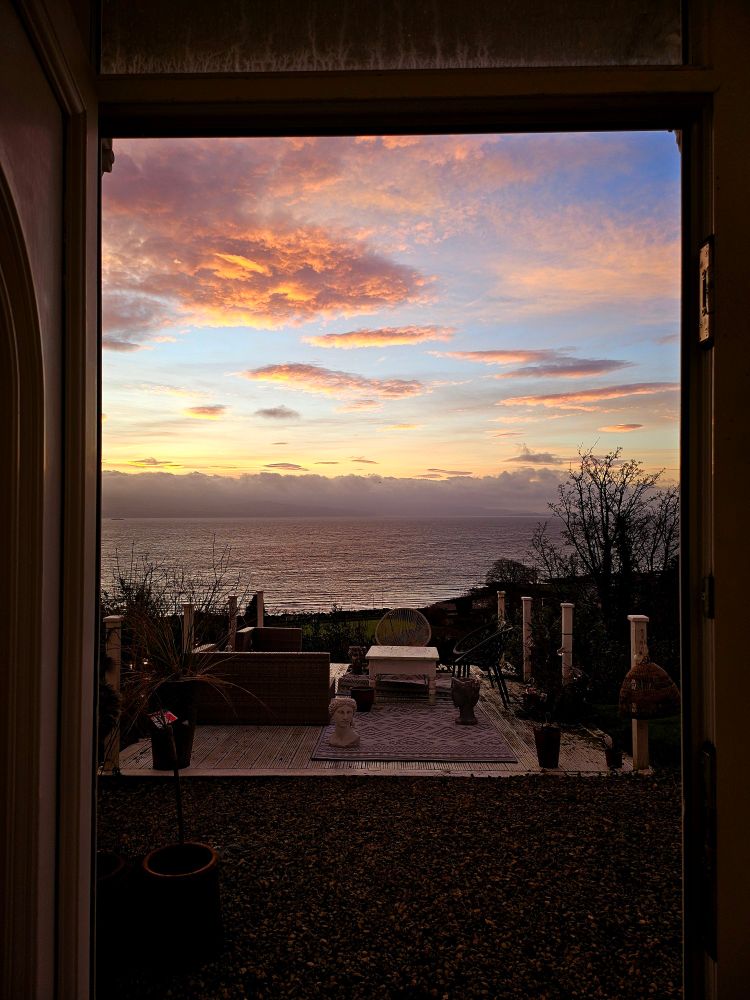 A view from my doorstep over the Firth of Clyde. Pink clouds are scattered across a blue and orange sky.