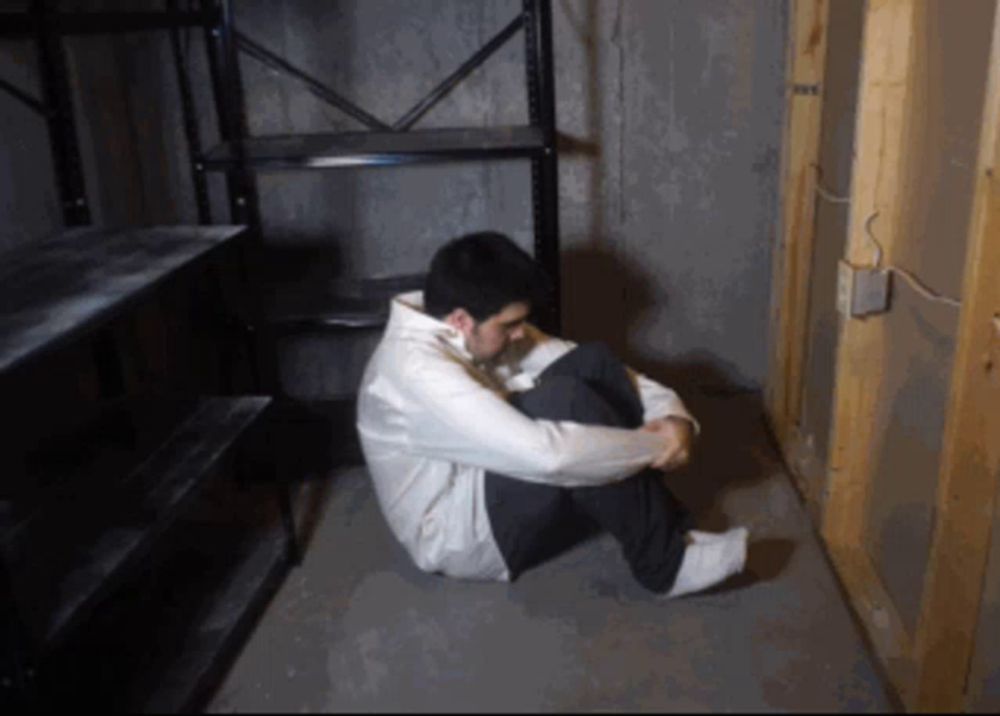 a man is sitting on the floor in a dark room with a shelf in the background