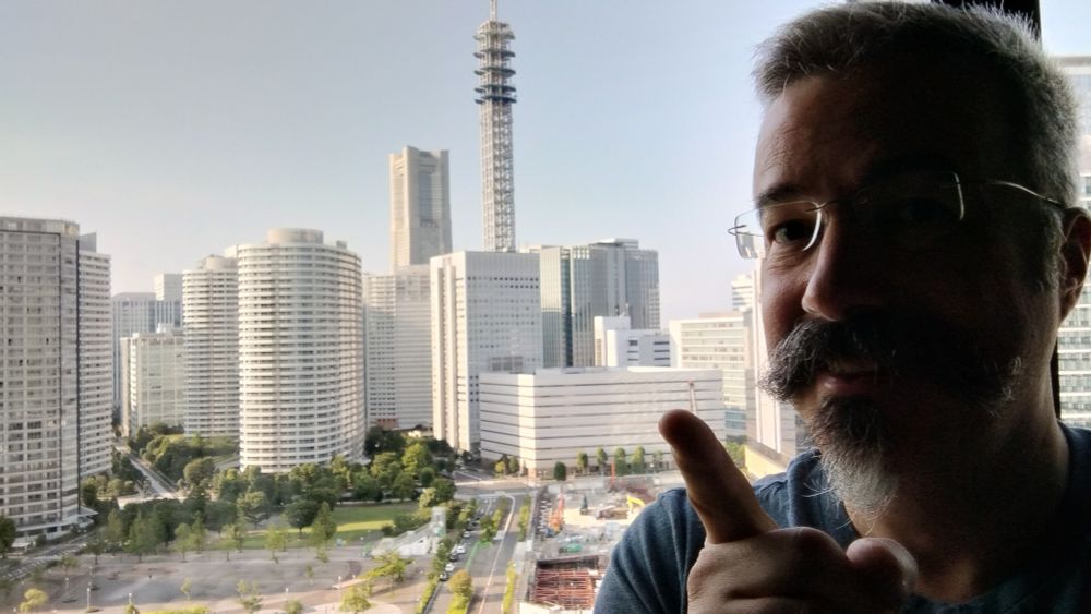 Tom Tobin smiles in front of a window overlooking a dense city landscape.