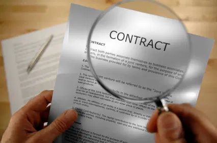Image of a person's hands holding a magnifying glass, looking at the heading "contract" in a printed document.