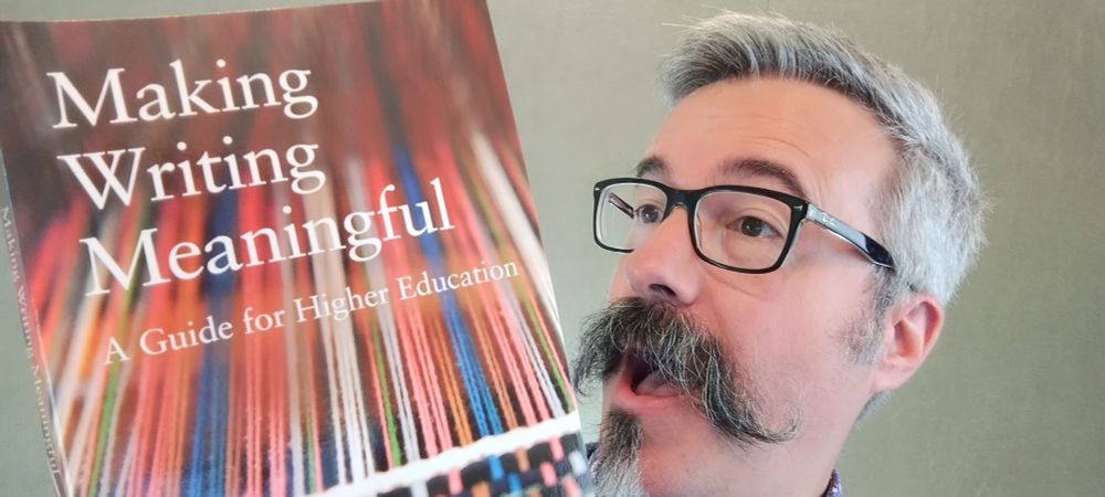 Close-up of Tom Tobin smiling as he reads "Making Writing Meaningful: A Guide for Higher Education."
