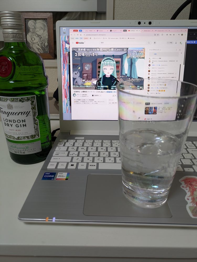タンカレーの瓶がテーブルに、氷と透明な液体の入ったコップがノートPCのマウスパッドに置かれ、ノートPCの画面には配信が映っている