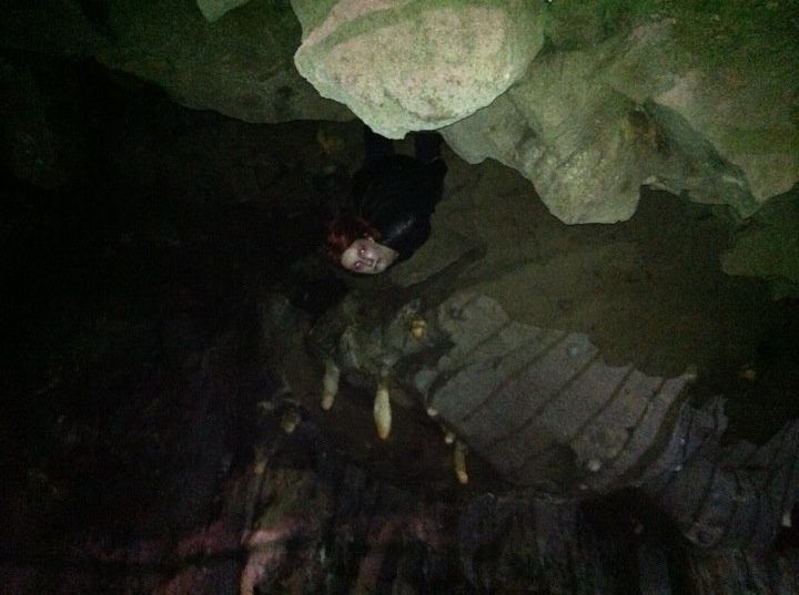 A dead-looking creature with red-rimmed eyes apparently hanging upside down from the roof of a cavern, surrounded by stalactites. 