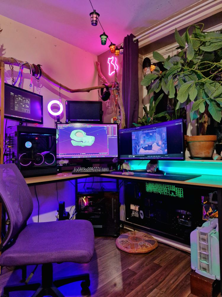 Neon themed workspace desk pc with cat neon sign above. Plants to the right. 