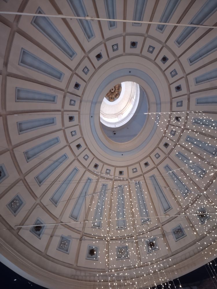 Looking upward at the dome in Quincy Market in Boston. It's a large dome with blue and white details and big wooden flowers at the top and bottom.