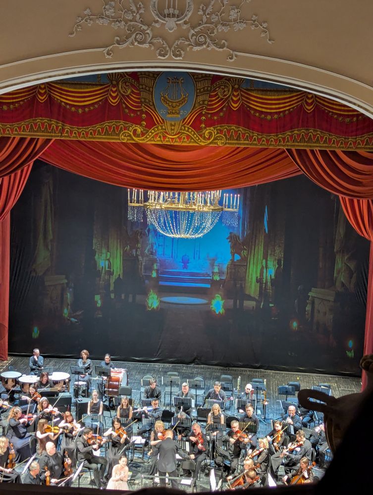 A view of an orchestra with a screenshot from dragon age inquisition in the background 