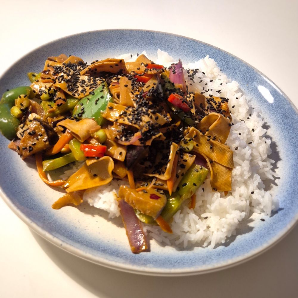 Teller mit Reis, gebratene Tofustreifen, grüne Paprika, Bambusstreifen, Aubergine, Karotte, Chili, schwarzem Sesam