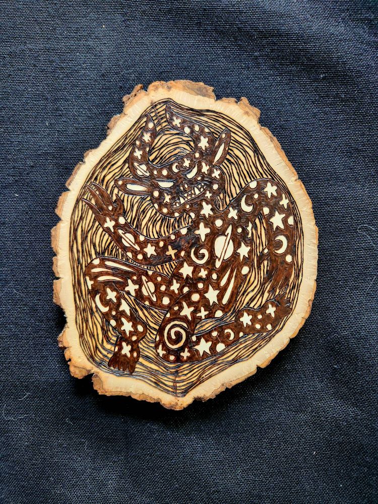 Wood burned art piece.  Shows a dark devil with a space pattern all over its body.  The background is wavy lines.
