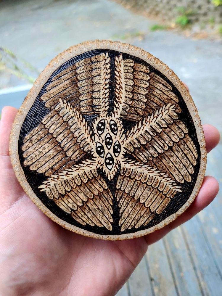 Wood burned art piece.  Shows a biblical angel. Six wings stem from a center mass with six eyes.