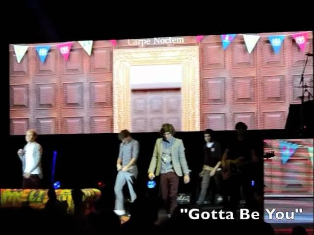 One direction on stage with a door in the background above which reads “Carpe Noctem.” In the corner overlaid, text reads “Gotta Be You.”