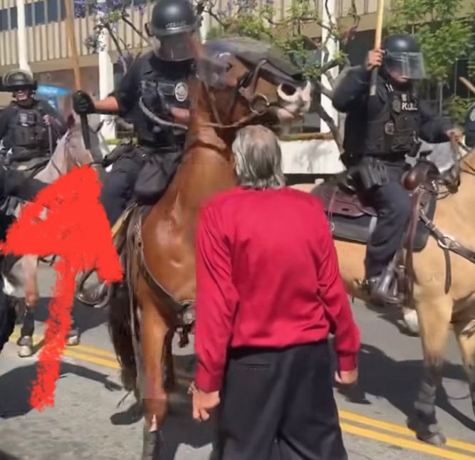 “Police” beating an elder with a wooden baton. Poised to swing at his head. 