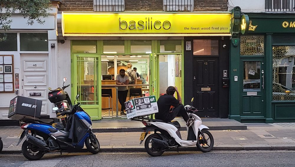 Pizza smotor. Night, with delivery drivers by the curb on motos.