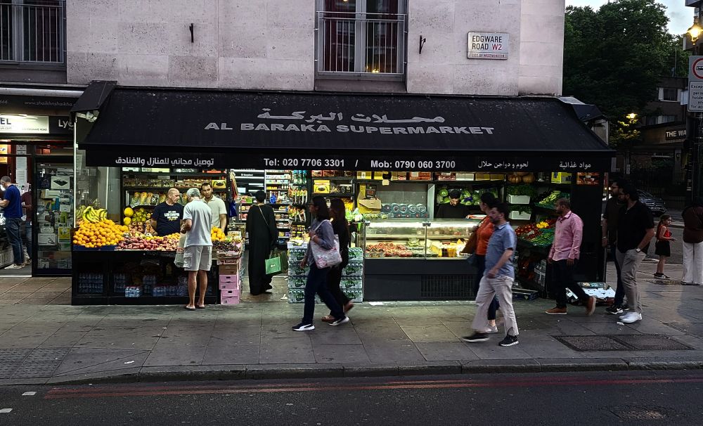 Arabic grocery storefront at night, with patrons and passers by, Edgeware Rd.