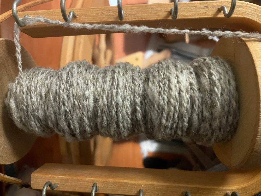 One large spinning wheel bobbin half filled with 2-ply grey Rambouillet yarn 