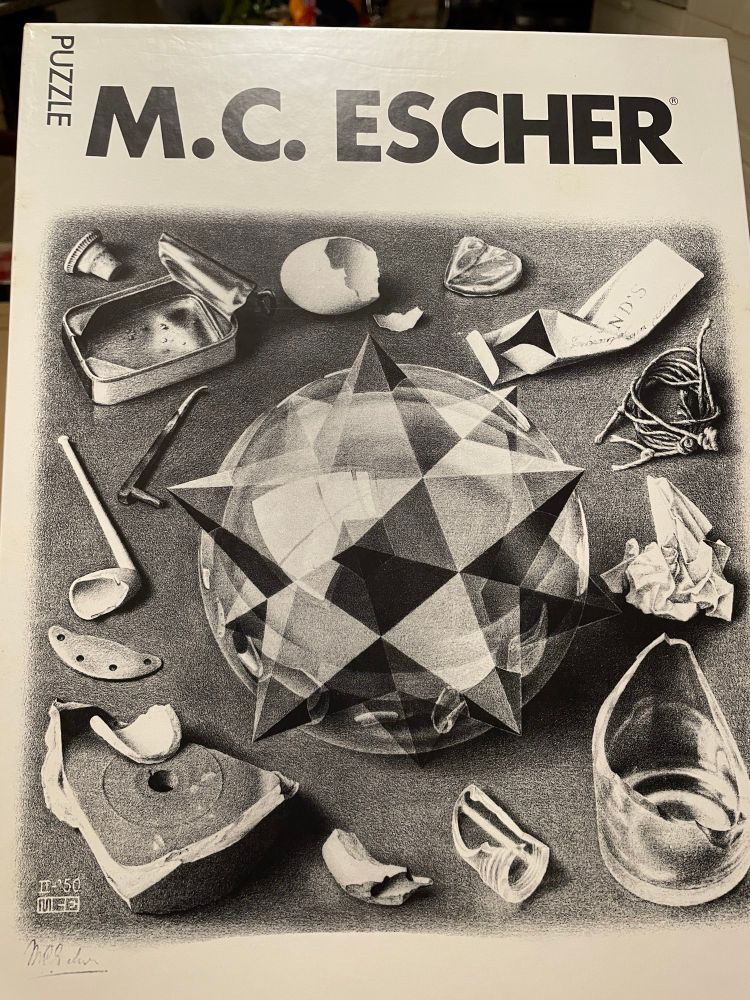A puzzle box that says MC Escher. The picture is “Order and Chaos”, which is a pencil drawing with many broken things arranged around a geometric sphere and star.
