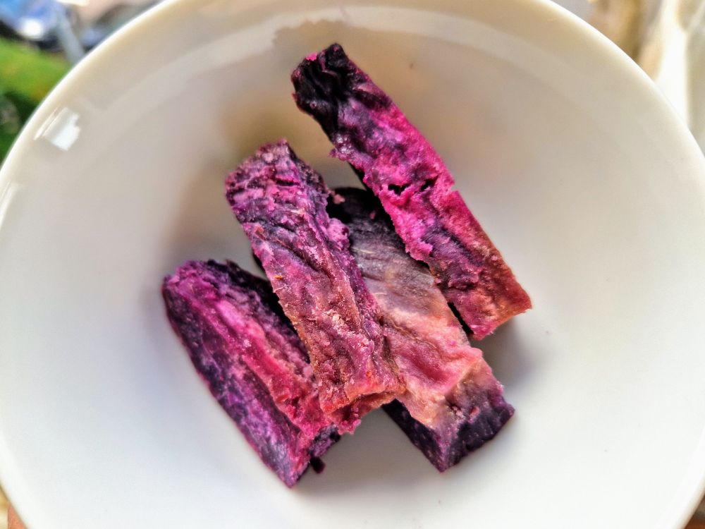 A small porcelain bowl with a few pieces of bright purple dried sweet potatoes.
