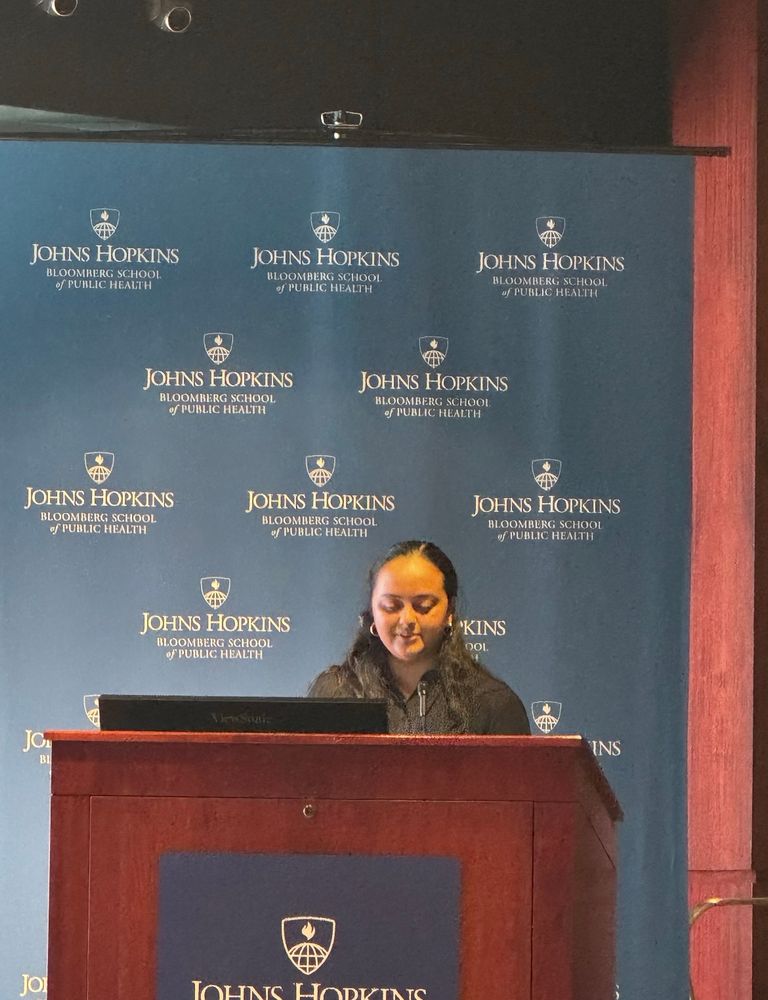 Jayati at a podium with the JHU logo in background